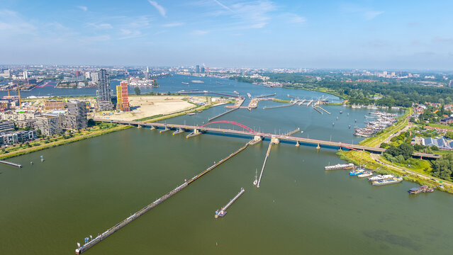 Aerial view of the Schellingwouderbrug bridge spanning the IJ river with boats moored along the banks and the urban skyline of Amsterdam, Amsterdam, North Holland, Netherlands.
