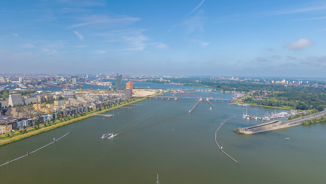 Aerial view of the IJ river featuring modern architecture, the bridge, and boats on the water under a clear blue sky Amsterdam, North Holland, Netherlands.