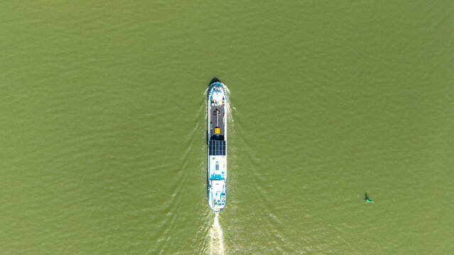 Aerial view of a cargo ship navigating through green water, creating a wake as it travels in Amsterdam, North Holland, Netherlands.