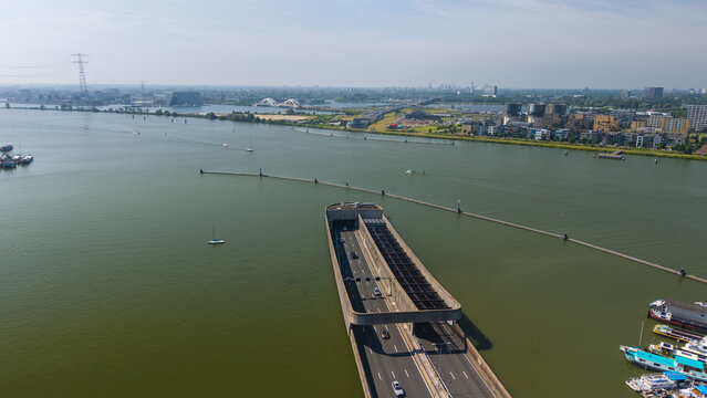Aerial view of the IJ waterway tunnel entrance with boats moored along the shore and the urban skyline in the distance in Amsterdam, North Holland, Netherlands.