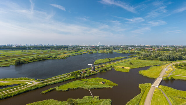 Aerial view of a traditional Dutch windmill situated amidst lush green wetlands and winding waterways near Amsterdam, North Holland, Netherlands.