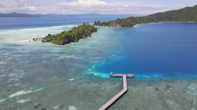 Aerial view of Yenbuba jetty extending into clear turquoise waters surrounded by lush tropical islands in Meos Mansar, Southwest Papua, Indonesia.