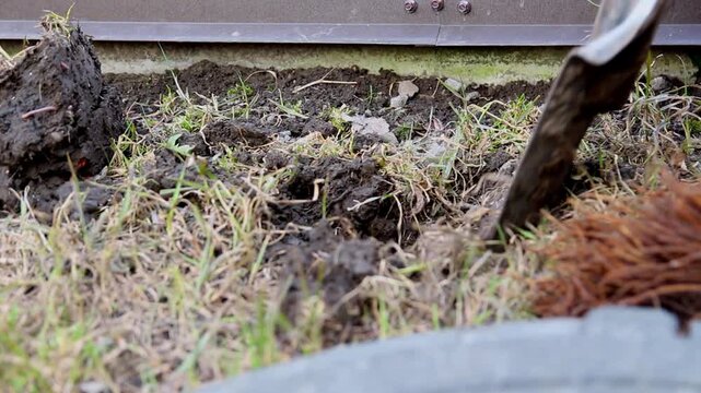 Close-up of a worker digging the ground with a shovel near a building foundation outdoors