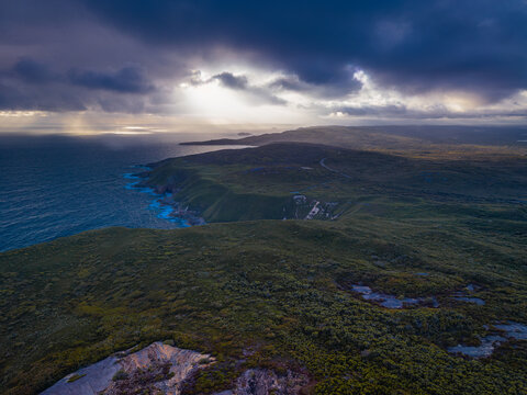 Aerial view of Stony Hill with rugged coastal cliffs, lush green vegetation, and dramatic sun rays over the Southern Ocean in Torndirrup, Western Australia, Australia.