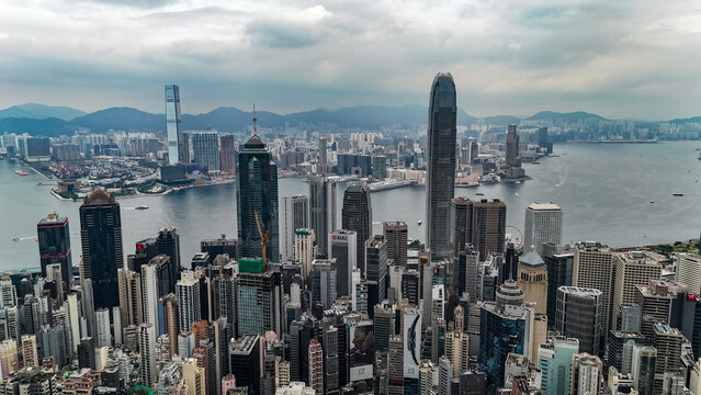 Hong Kong, Hong Kong - 12 July 2026: Aerial view of the dense Hong Kong skyline featuring iconic skyscrapers, Victoria Harbour, and surrounding mountains under a cloudy sky.