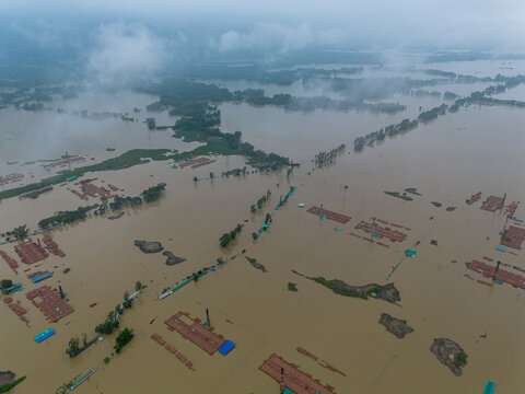 Aerial view of flooded industrial buildings and landscape partially submerged in muddy water under a cloudy sky in Satkania Upazila, Chittagong Division, Bangladesh.