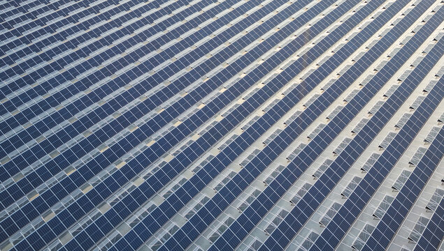 Aerial view of solar panels and greenhouse skylights forming an abstract geometric pattern on a large commercial greenhouse roof in Saulce-sur-Rhone, Auvergne-Rhone-Alpes, France.