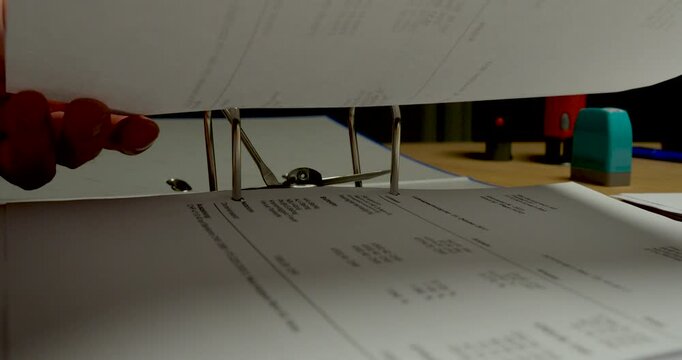 Close-up of hole-punched documents being inserted into a ring binder. Ideal for document organization, filing, office administration, record keeping, and paperwork management concepts.