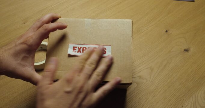 Close-up of hands applying an "EXPRESS" shipping label to a cardboard parcel. Ideal for express delivery, priority shipping, logistics, ecommerce, and fast shipping concepts.