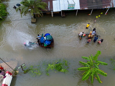 Banshkhali Upazila, Chittagong Division, Bangladesh - 10 July 2026: Aerial view of flooded streets with people wading through water and a vehicle with umbrellas, near submerged homes.