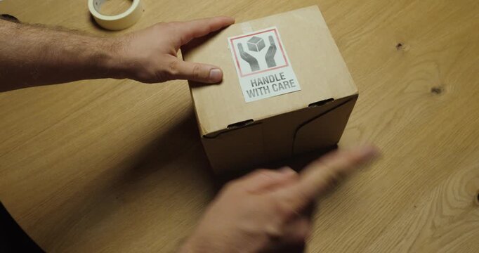Demonstration of improper package handling by dropping a parcel despite a "Handle with Care" label, followed by pointing at the warning label. Ideal for shipping safety, warehouse training, logistics,