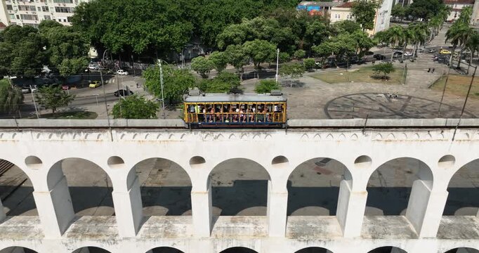 Aerial view of the historic Arcos da Lapa aqueduct with a yellow tram crossing it, surrounded by urban greenery and city streets in Rio de Janeiro, State of Rio de Janeiro, Brazil.