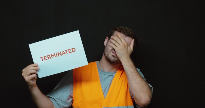Worker holding a "TERMINATED" sign while covering his face in disappointment. Ideal for job loss, unemployment, layoffs, dismissal, and workplace crisis concepts.