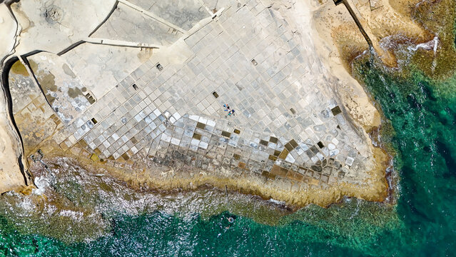 Aerial view of Malta salt pans beside blue Mediterranean water on sunny coast