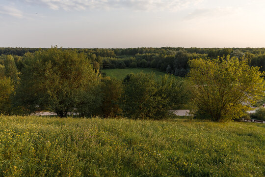 Warm golden hour sunlight illuminates a lush green hill meadow and dense forest trees in Park im. Cichociemnych Spadochroniarzy AK at Gorka Kazoora, creating a scenic park landscape in Warsaw, Poland.
