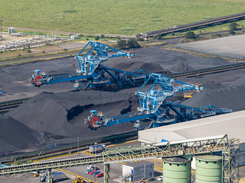 Aerial view of large blue bucket wheel excavators operating at a coal storage facility with massive piles of coal, conveyor systems, and industrial infrastructure in the United Kingdom.
