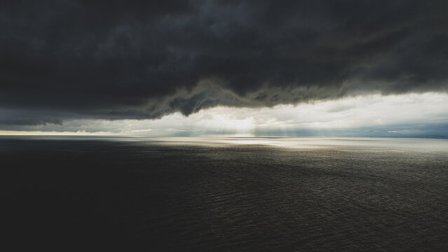Aerial view of the vast ocean under dark, dramatic storm clouds with rays of light breaking through the horizon in Japan.