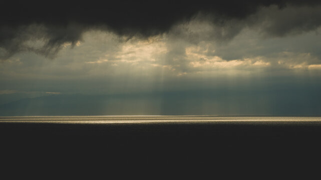 Aerial view of dramatic sunbeams breaking through dark storm clouds over the sea in Japan.
