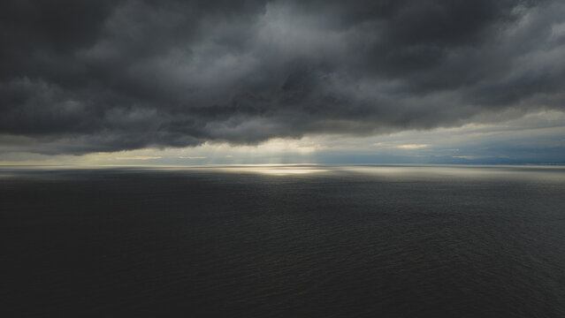 Aerial view of dark storm clouds over the ocean with dramatic light rays breaking through the horizon in Japan.