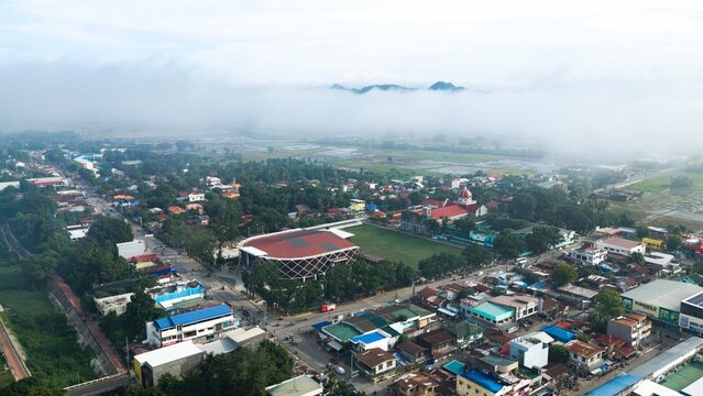 Barotac Nuevo, Philippines - 08 July 2026: Aerial view of the town center with its church, red dome, sports complex, residential buildings, and lush greenery under a misty sky.