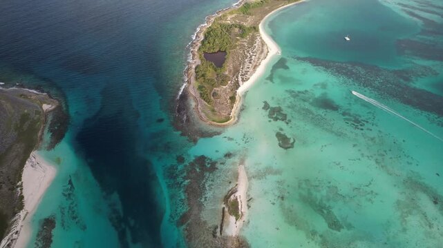 Aerial view of Los Roques archipelago with turquoise waters, coral reefs, and a small boat moving through the Caribbean Sea in Los Roques, Los Roques, Venezuela.