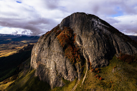 Aerial view of the rugged rock face of Cerro Mackay with autumn foliage and dramatic clouds in the valley near Coyhaique, Aysen, Chile.