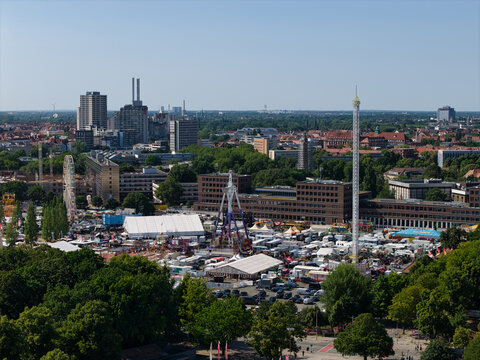 Hanover, Germany - 12 July 2026: Aerial view of the Schutzenfest fairgrounds near Maschsee, featuring amusement rides, white tents, and carnival attractions set against the urban skyline.