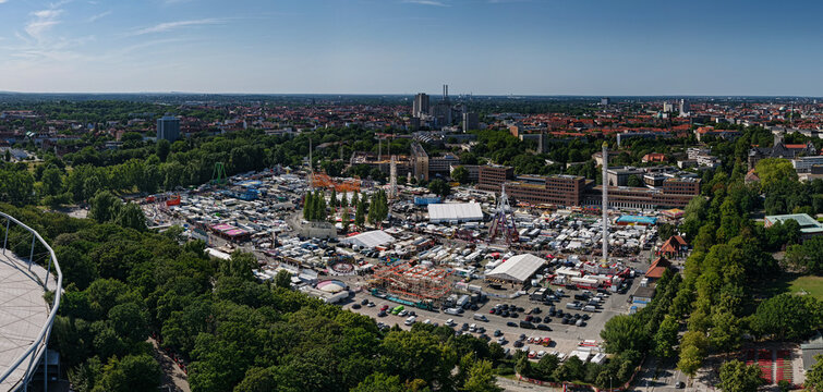 Hanover, Lower Saxony, Germany - 12 July 2026: Aerial view of the fairground near Maschsee, featuring amusement rides, white tents, and parking areas surrounded by lush trees.