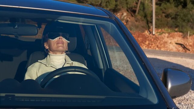 Tired woman sleeping inside car with eye mask. Tired woman sitting in the driver's seat of her parked car puts on a sleep mask to take a relaxing nap during a break on a long road trip