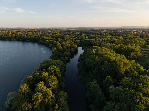 Aerial view of Maschsee surrounded by lush green trees and calm water during the golden hour in Hanover, Lower Saxony, Germany.