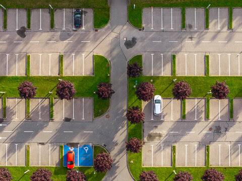 Aerial view of a parking lot with marked spaces, green grass strips, small trees, and a few parked cars in Pruszkow, Mazowieckie, Poland.