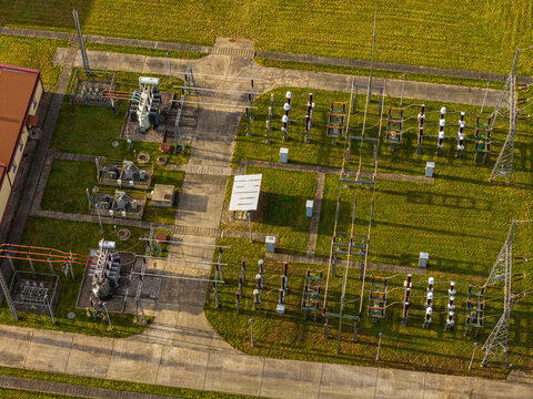 Aerial view of an electrical substation featuring transformers, power lines, and switchgear equipment situated on a grassy field in Poland.
