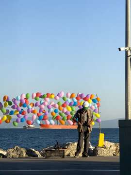 View of a man standing by the sea with a large display of colorful balloons and a cargo ship in the background in Avcilar, Istanbul, Turkiye.