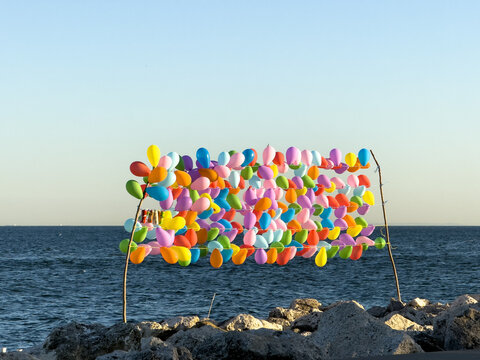 View of a colorful display of balloons tied to a wooden frame on a rocky shoreline against the sea in Avcilar, Istanbul, Turkiye.