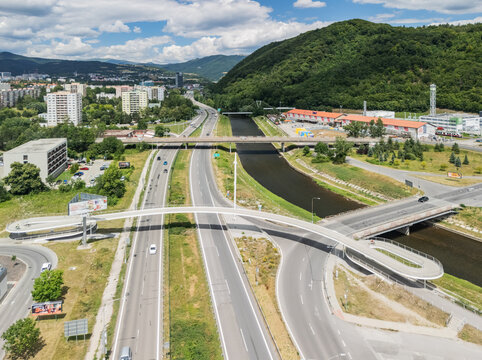 Aerial view of the R1 motorway crossing the Hron river with a modern pedestrian bridge and surrounding urban landscape in Banska Bystrica, Banska Bystrica Region, Slovakia.