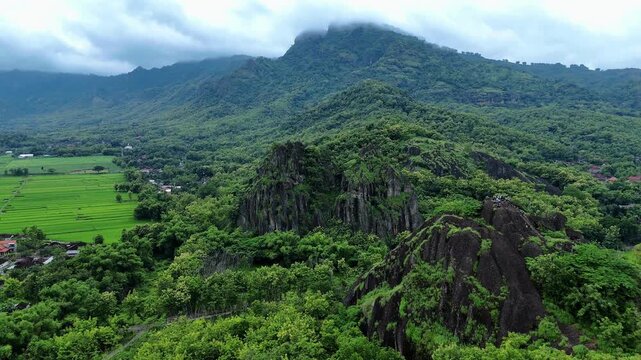Aerial view of Gunung Sepikul Sukoharjo featuring rugged rock formations surrounded by lush green forests and vibrant rice paddies in Kecamatan Bulu, Jawa Tengah, Indonesia.