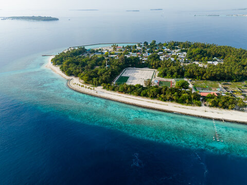 Aerial view of Kihaadhoo island featuring lush tropical vegetation, a soccer field, and white sandy beaches surrounded by a turquoise lagoon and coral reef in Kihaadhoo, Baa Atoll, Maldives.