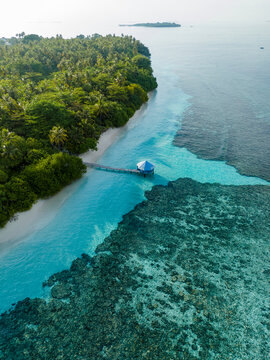 Aerial view of Kihaadhoo island, showing a wooden pier extending into the turquoise lagoon, surrounded by lush tropical vegetation and vibrant coral reefs. Kihaadhoo, Baa Atoll, Maldives.