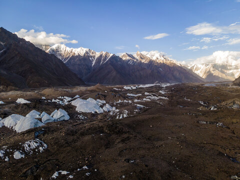 Aerial view of Goro II campsite featuring rugged glacial terrain, scattered ice formations, and towering snow-capped peaks under a clear blue sky, Goro II, Gilgit Baltistan, Pakistan.