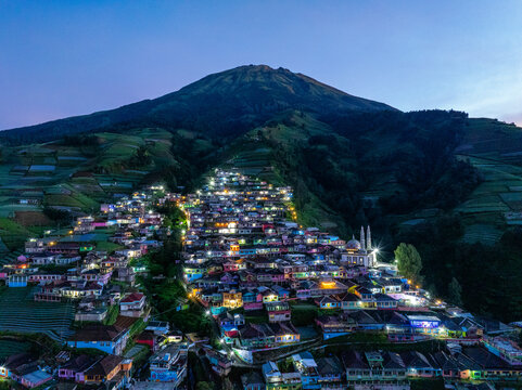 Aerial view of Nepal Van Java village nestled on the slopes of Mount Sumbing with colorful houses illuminated at night in Kecamatan Kaliangkrik, Jawa Tengah, Indonesia.