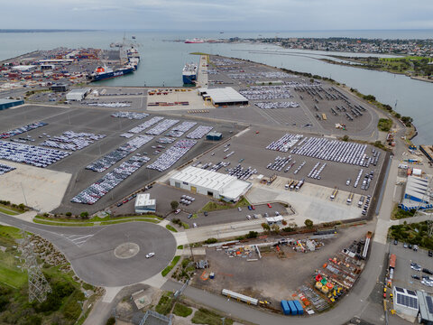 Port Melbourne, Australia - 01 April 2026: Aerial view of the Port of Melbourne featuring extensive car storage lots filled with vehicles, shipping terminals, and industrial infrastructure.