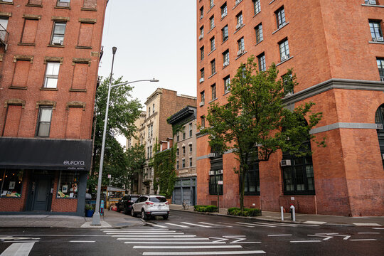 New York City, New York, USA - 08.04.2024: A red brick building stands at a Manhattan street corner with a salon storefront on the ground floor. Wet pavement, parked cars, and urban architecture