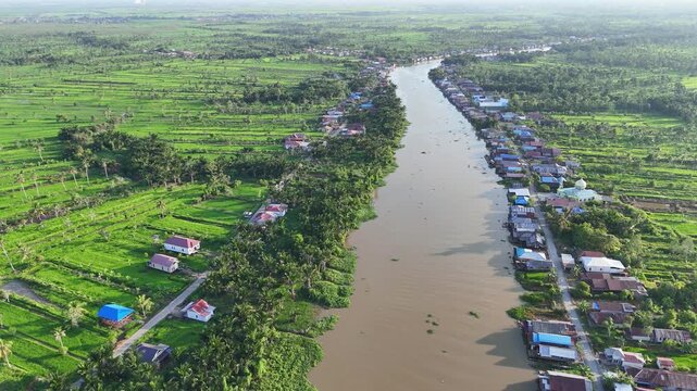 Aerial view of the Martapura River winding through lush green rice fields and rural houses in Sungai Tabuk, South Kalimantan, Indonesia.
