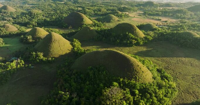Aerial view of the iconic conical Chocolate Hills covered in lush green grass during golden hour in Batuan, Central Visayas, Philippines.