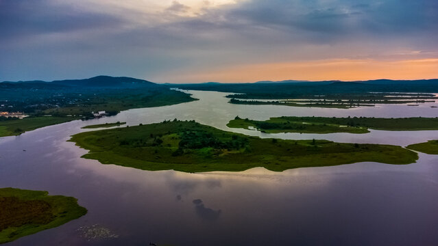 Aerial view of the Volta River winding through lush islands and wetlands at sunset in Kpong, Eastern Region, Ghana.