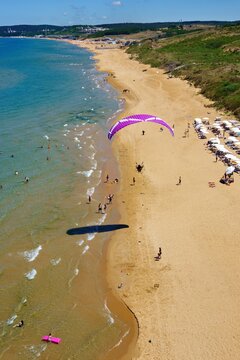 Aerial view of a paraglider soaring above the sandy beach of Kisirkaya with sunbathers and swimmers along the coastline in Sariyer, Istanbul, Turkey.