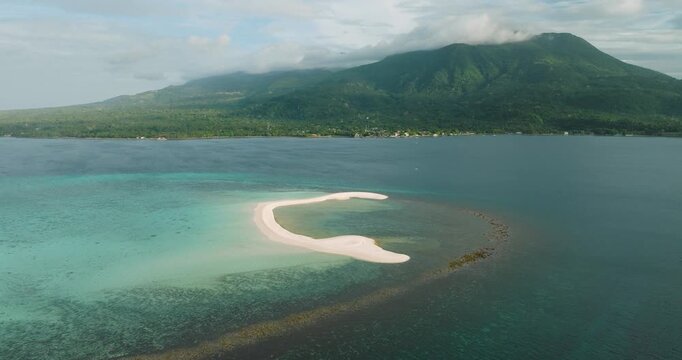 Aerial view of the pristine white sandbar of White Island surrounded by turquoise waters and the lush green mountains of Camiguin in Mambajao, Camiguin, Philippines.