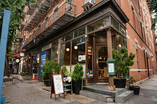 New York City, New York, USA - 08.04.2024: A corner restaurant entrance with large windows and potted plants sits along a Manhattan street. Historic brick architecture and outdoor signage create a