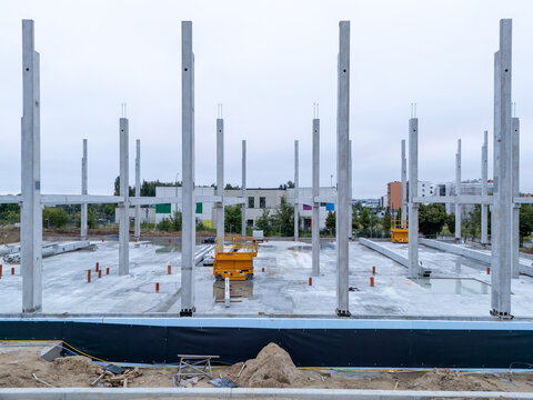 Aerial view of a construction site featuring concrete pillars and a foundation with a yellow scissor lift under an overcast sky in Gdansk, Pomeranian Voivodeship, Poland.