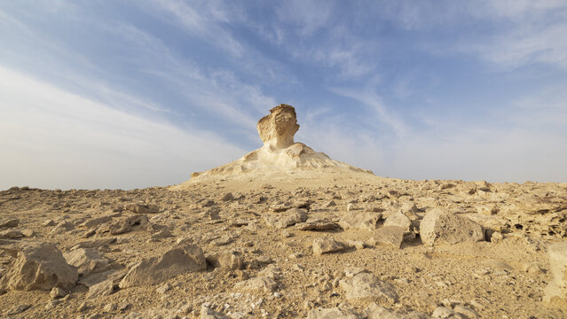 View of the Zekreet Rock Formation rising from the arid desert landscape with scattered rocks under a clear blue sky in Zekreet, Al Sheehaniya Municip, Qatar.
